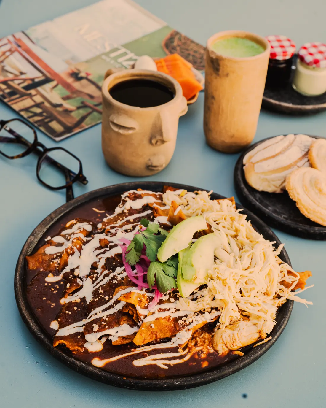 Chilaquiles xiqueños bañados en mole, con pollo, queso, crema, aguacate y cebolla curtida, servidos en plato de barro negro
