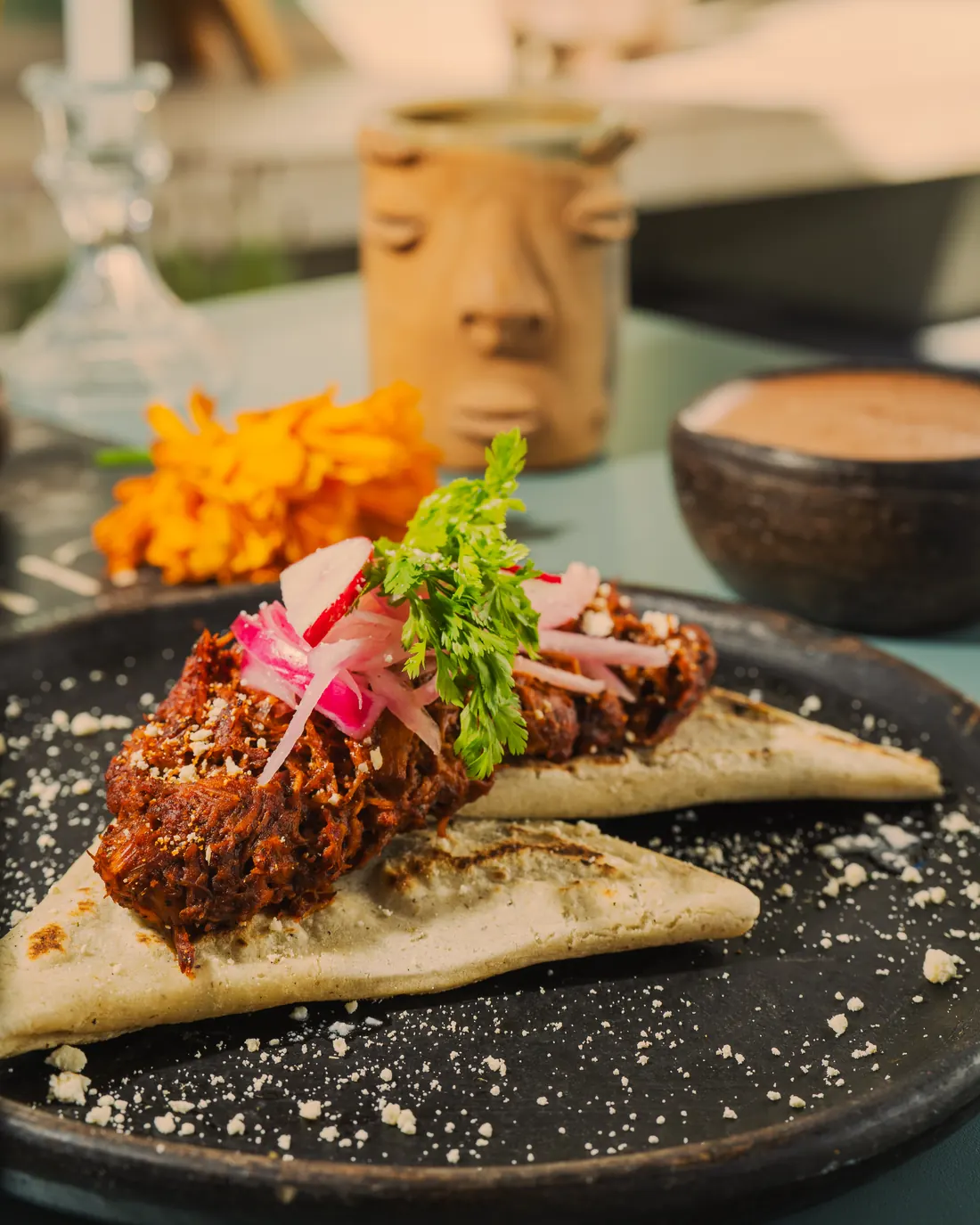 Tetelas yucatecas de tortilla de maíz rellenas de frijoles, con cochinita pibil, cebolla curtida, rábano y queso, servidas en plato de barro negro
